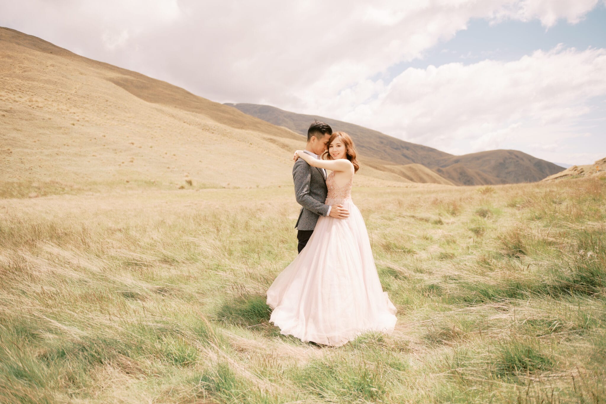 Queenstown Tekapo New Zealand Heli Wedding Elopement Pre-Wedding Shoot Photographer クイーンズタウン　テカポ　ニュージーランド　エロープメント 前撮り　フォトウェディング　結婚式 | A couple embracing in a field with rolling hills in the background during their Tekapo pre-wedding shoot.